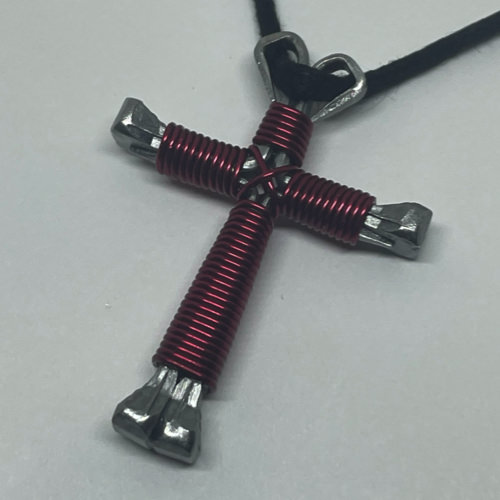 A small magenta cross of nails necklace on a black cord.
