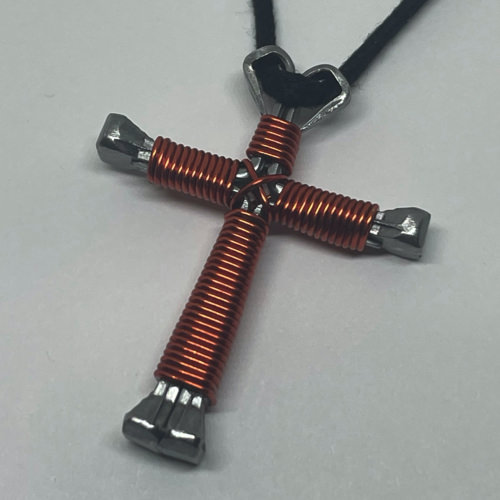 A small orange cross of nails necklace on a black cord.